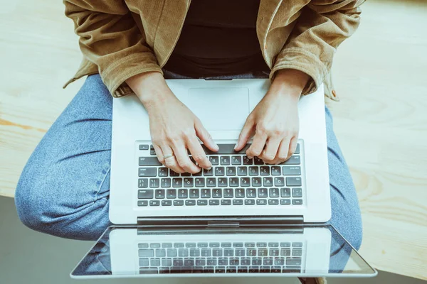 Vrouwen typen op laptop toetsenbord zittend op houten vensterbank. Vrouw in casual met behulp van computer. Hoge hoek uitzicht. Dichtbij schot. Getinte afbeelding — Stockfoto