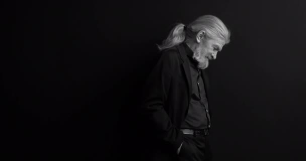 Old business man with long hair and beard in dark business clothes standing sideways in semi-lit room on black background. Black and white portrait. Waist portrait. Prores 422 — Stock Video