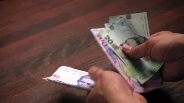 Mans ruce počítání ukrajinských Hryvna peníze. Mužské ruce drží balíček nových ukrajinských bankovek, na dřevěném podstavci stolu. Koncept hotovostních peněz. Investiční koncept. Záběr zblízka. Prores 422 — Stock video