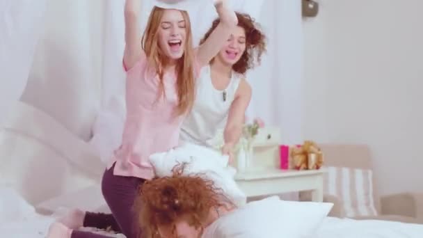 Pillow fight charmantes filles passent du temps libre à la maison en pyjama confortable. Trois femmes heureuses meilleures amies allongées sur le lit et regardant la caméra. Concept d'amis. Prores 422 — Video