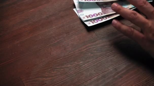 Mans kézzel bizalmatlan bankjegy a fa asztal sarkán. A kaukázusi férfinak új ukrán hrivnyái vannak fából készült asztal hátterével szemben. Közelről. Készpénz koncepció. Gyümölcsfélék — Stock videók