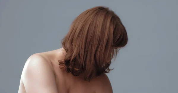 Μια θλιμμένη γυμνή γυναίκα κατέβασε το κεφάλι της, καλύπτοντας το πρόσωπό της με μαλλιά. Μια γυναίκα με κόκκινα μαλλιά σε γκρι φόντο. Έννοια της διαδικασίας γήρανσης. Μοναχική έννοια — Φωτογραφία Αρχείου