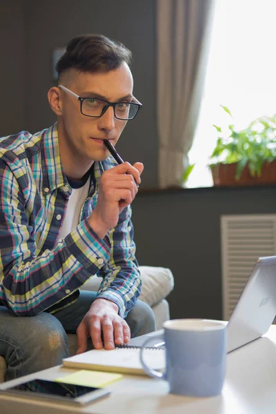 Un joven que trabaja por cuenta propia. Retrato del tipo caucásico sentado en el lugar de trabajo. Hombre en gafas con cara reflexiva — Foto de Stock