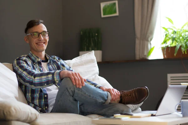 Happy freelancer se relaja durante el proceso de trabajo sentado en el sofá. Sonriente joven tener descanso descanso y trabajar en casa — Foto de Stock