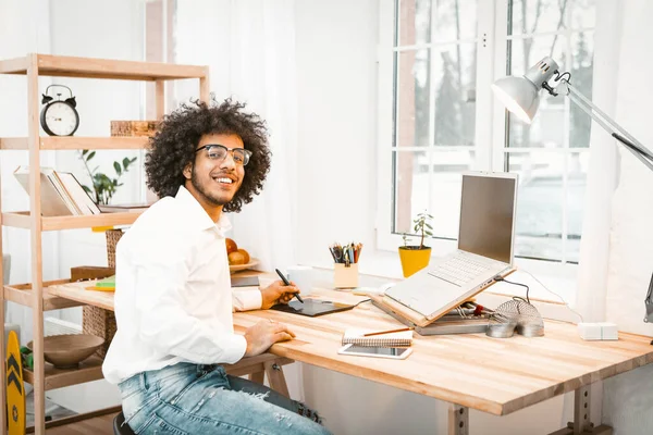 Freelanser inteligente sonríe ante la cámara sentada en su lugar de trabajo. Joven empresario creativo trabajando desde casa. Trabajo a distancia o concepto de trabajo remoto. Imagen tonificada — Foto de Stock