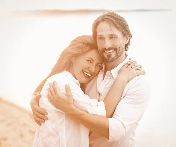 Bella coppia stare abbracciando sullo sfondo del mare o dell'oceano. Uomo e donna sorridenti in abiti bianchi che si abbracciano. Immagine colorata — Foto Stock