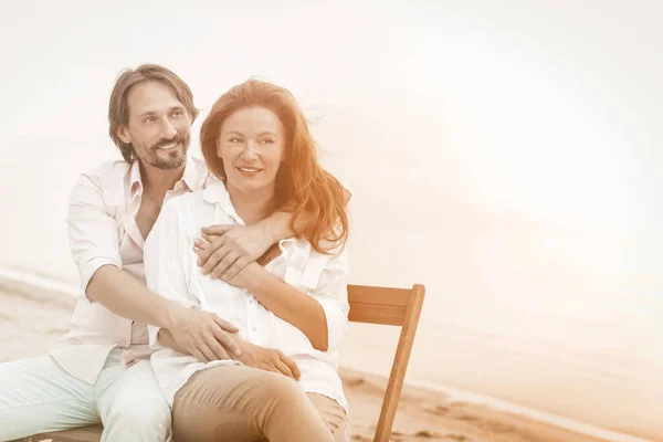 Gelukkig volwassen stel knuffels zittend in strand cafe aan zee. Portret van het knuffelen van mooie twee mensen die verliefd zijn op kopieerruimte aan de rechterkant. Getinte afbeelding — Stockfoto