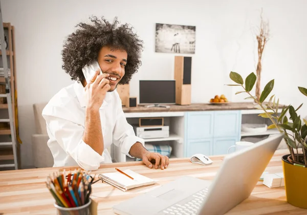 Encantador joven empresario habla por teléfono inteligente o móvil mirando a la cámara durante el trabajo desde casa. Imagen teñida — Foto de Stock