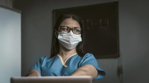 Trött sjukvårdare ser tankfullt på sidan. Pensiv kvinnlig läkare tror att sitta vid skrivbordet med laptop på. Ett pandemiskt koncept. Tonad bild — Stockfoto