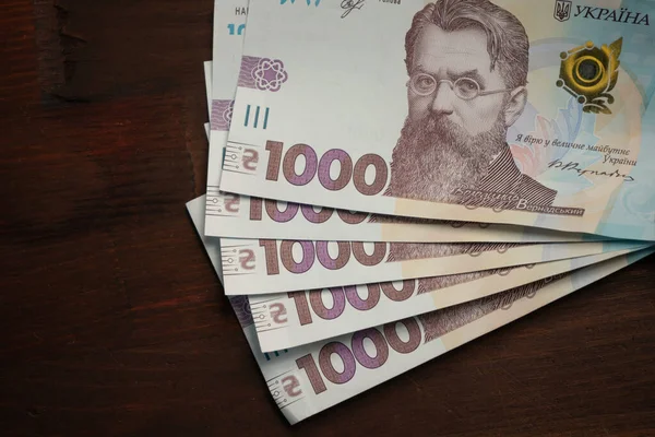 Нові українські паперові гроші номіналом 1000 гривень на дерев'яному столі з вбудованим темпом для лівого тексту. Закріплений постріл. Високий кут. — стокове фото