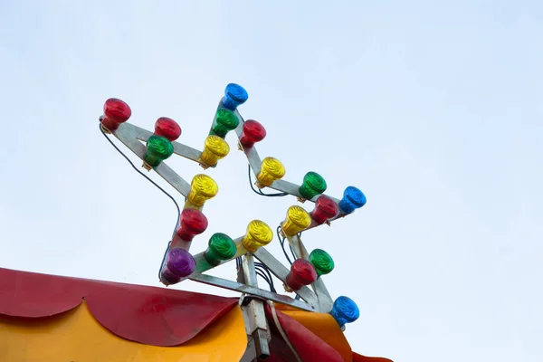 Star-shaped lamp with multi-colored light bulbs at top of circus or carousel. Illumination against sky background. Entertainment concept — Stock Photo, Image