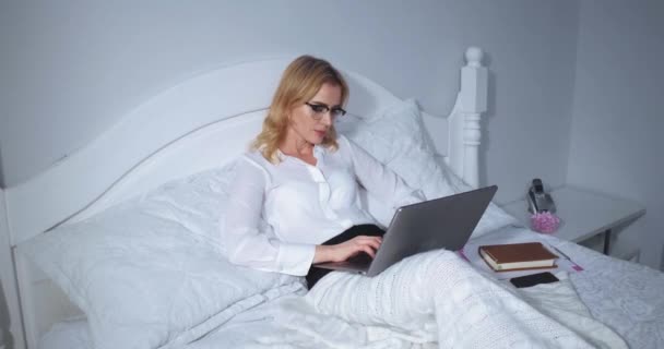 Késő este, egy szabadúszó nő dolgozik egy laptopon egy hotelszobában egy hosszú repülés után. Szabadúszó nő dolgozik az ágyban. Üzleti koncepció. Hangfelvétel. Gyümölcsfélék — Stock videók