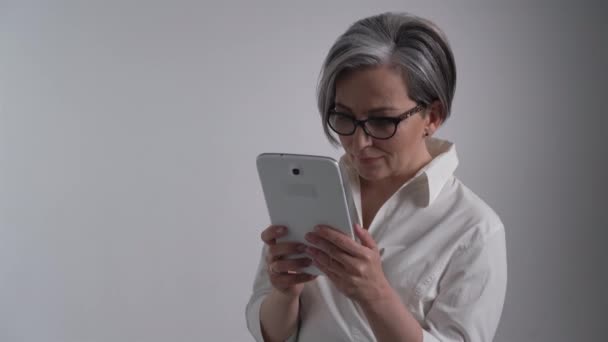 De cerca. Mujer de negocios alegre trabaja en tableta digital sobre fondo blanco. Señora madura en blanco mirando a la cámara. Concepto de empresa o educación. Prores 422 — Vídeo de stock