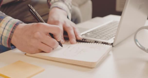 Νέος ελεύθερος επαγγελματίας σπουδάζει ενώ εργάζεται μακριά στο σπίτι χρησιμοποιώντας το laptop για την εργασία και την εκπαίδευση. Κοντινό πλάνο για τη συγγραφή μαθηματικής λύσης στο βιβλίο αντιγράφων. Επιχειρηματική ιδέα. Πρότυπα 422. — Αρχείο Βίντεο