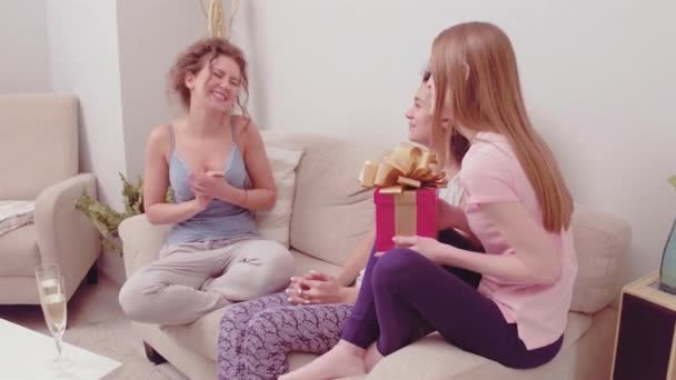 Two girls giving present to a friend. Celebrate party with champagne and cookies. Pajamas party. Beautiful girl is surprised with present. Toned footage. Prores 422 — Stock Video