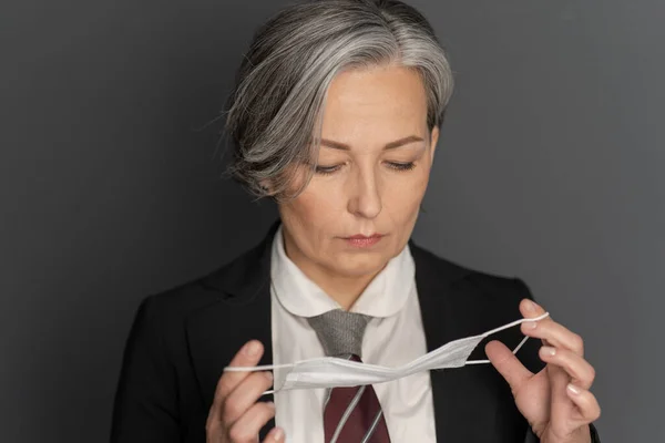 Mulher de negócios de cabelos grisalhos, a pôr uma máscara protectora no rosto, a olhar para baixo. Fecha o retrato. Conceito pandêmico. Conceito de protecção — Fotografia de Stock