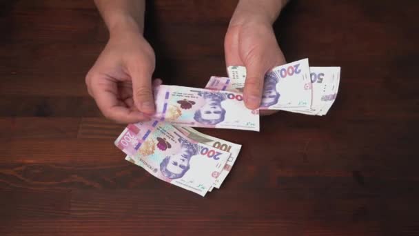 Le mani dell'uomo contano il controllo delle nuove banconote ucraine. Le nuove grivne di carta il valore nominale diverso sono su un tavolo di legno marrone. Concetto di denaro liquido. proporzioni 422 — Video Stock
