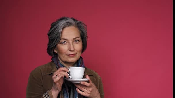 Koffie tijd concept. Charmant blank grijs-harige vrouw drinkt koffie in witte beker op een roze achtergrond in de studio. Sluit de beelden. Prores 422 — Stockvideo