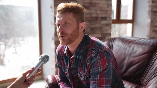 Gorgeous man giving interview talking in microphone in his house in living room. Young attractive guy having conversation with news reporter talking into microphone at home. Prores 422 — Stock Video