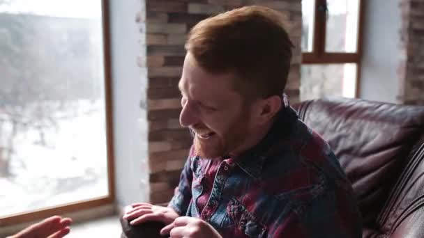 A blogger laugh at a journalist question sitting in a chair near a window overlooking a snowy courtyard. A young designer gives interviews answering questions. Prores 422 — Stock Video