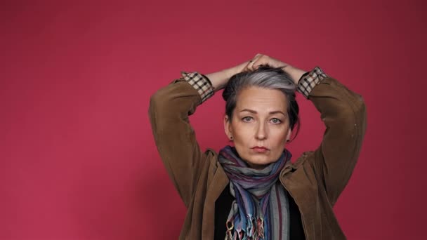 Sexy mujer de pelo plateado mira a la cámara. Señora madura de buen aspecto en bufanda de varios colores posando en el estudio sobre fondo rosa. Prores 422 — Vídeos de Stock