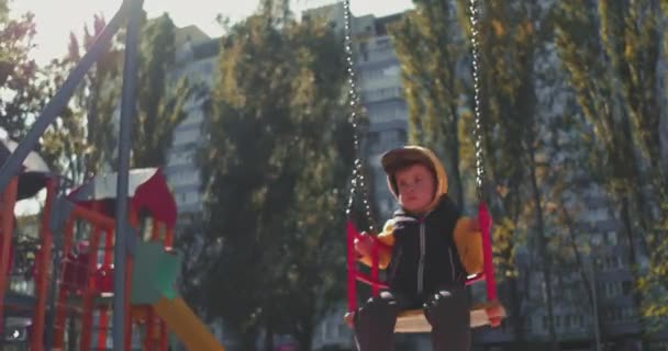Egy kisfiú hintázik a ház melletti parkban, egy fiú játszik a játszótéren, a boldog fiú hintázik. Gyümölcsfélék — Stock videók