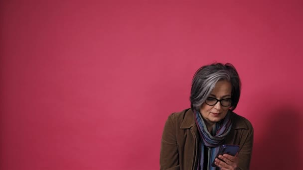 Gråtande vacker kvinna ta telefonen ner leenden. Smart mogen dam i glasögon och brun jacka på rosa bakgrund. Text utrymme på vänster sida. Prores 422 — Stockvideo