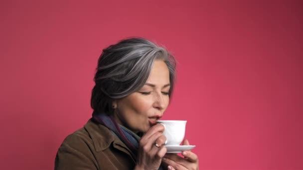 Charmante Kaukasierin trinkt Kaffee mit weißer Tasse. Ziemlich reife Dame lächelt leicht isoliert auf rosa Hintergrund. Beauty-Konzept. Kaffee-Zeit-Konzept. Prores 422 — Stockvideo