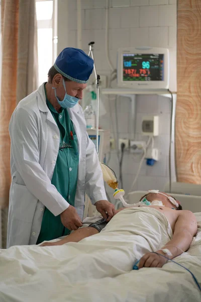 医者は重病患者を診察する。手術後の男は集中治療室にいる。市立病院。5月, 2020,ブロヴァリ,ウクライナ — ストック写真