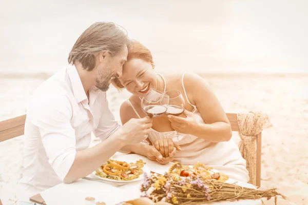 Sjarmerende ektepar som drikker vin på sjøsiden. To smilende hvite mennesker tilbringer tid sammen på strandkafeen. Kjærlighetskonsept. Jubileumskonsept. Merket bilde – stockfoto