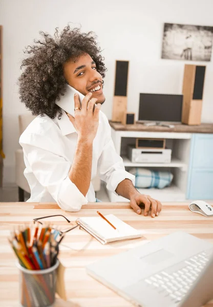 Happy entrepreneur parle mobile de travail de la maison. Charmant jeune homme regarde la caméra en utilisant le téléphone tout en étant assis au travail à la maison. Concept de style de vie. Image teintée — Photo