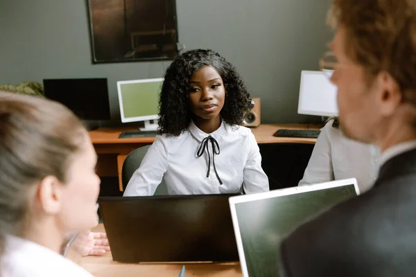 Mujer africana seria escucha atentamente a sus colegas Joven mujer de negocios en la reunión de negocios. Imagen tonificada —  Fotos de Stock