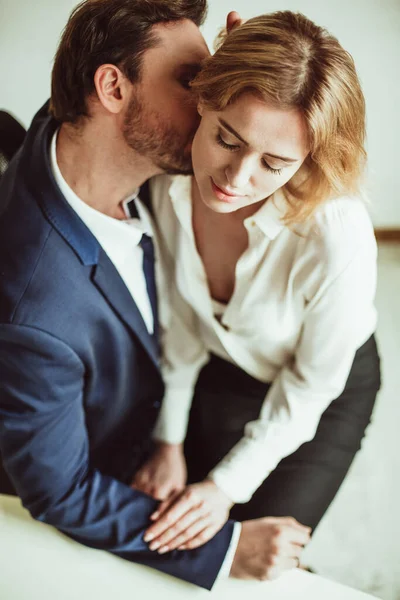 Dragoste la locul de muncă. Un om de afaceri sărută gâtul unei femei care stă în poala lui. Doi oameni flirtează împreună la birou. Vedere unghiulară — Fotografie, imagine de stoc