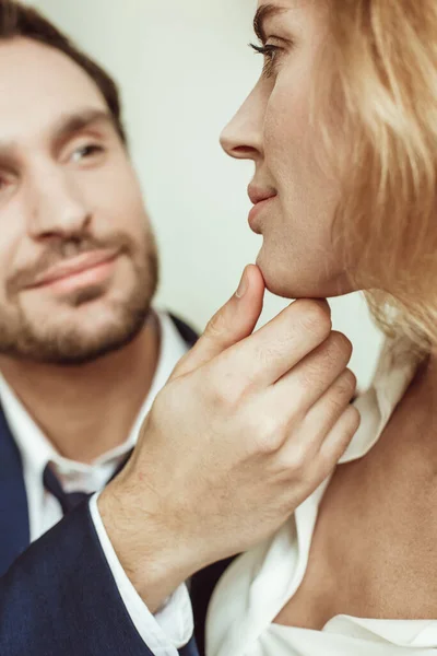 Feche o retrato do par apaixonado que olha um a outro. Homem a tocar no rosto feminino. Foco seletivo na mão masculina e perfil loiro sexy em primeiro plano — Fotografia de Stock