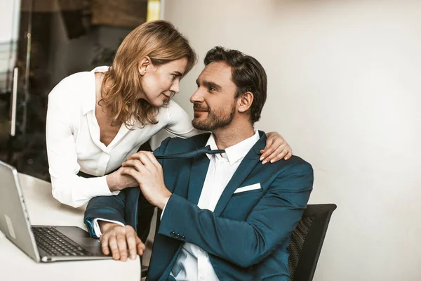 Förför kollegor på kontoret. Sexig blond kvinna flörtar med stilig leende affärsman drar honom i en slips och ser honom i ögonen. Tonad bild — Stockfoto