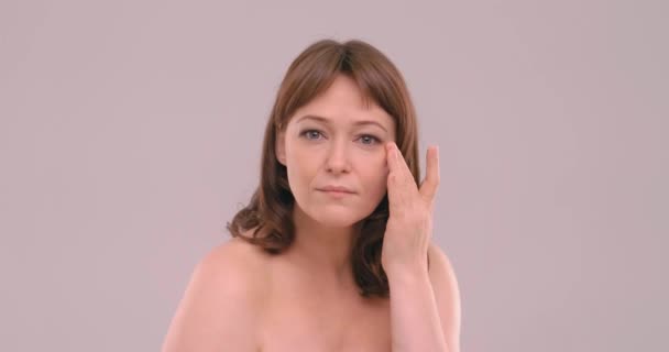 매력적 인 성숙 한 여성 이 낮에 얼굴 크림을 사용 해 완벽 한 부드러운 얼굴 피부를 눈 밑에 만지고 있습니다. 베이게 (beige) 에서 고립된 피부에 항산성 크림을 바르는 여성입니다. 프로방스 422 — 비디오