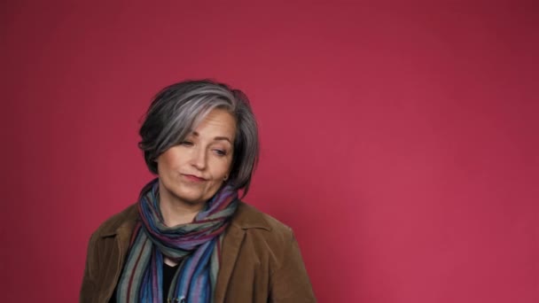 Mujer de pelo plateado fingiendo inocencia posando en cámara. Señora madura de buen aspecto en bufanda de colores posando en el estudio sobre fondo rosa. Prores 422 — Vídeos de Stock