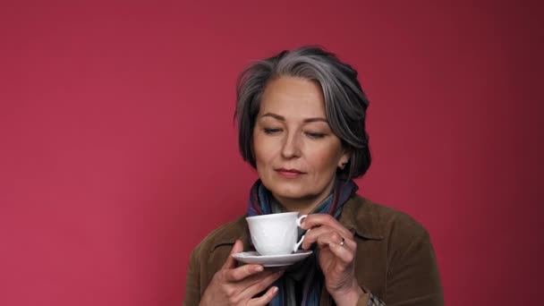 Nachdenkliche, charmante Frau mit Tasse Kaffee und weißer Tasse. Ziemlich reife Dame lächelt leicht isoliert auf rosa Hintergrund. Beauty-Konzept. Kaffee-Zeit-Konzept. Prores 422 — Stockvideo