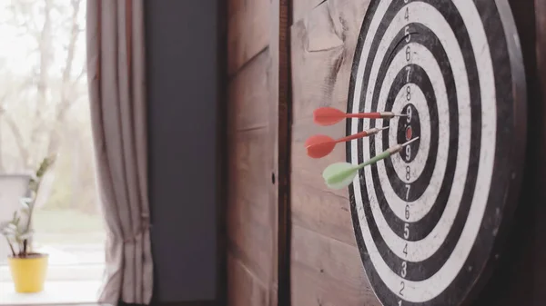 Three Darts arrows hit the bullseye. Dart board hanging on a wooden wall of home or office. Hit goal or target concept. Close up shot. Tinted image — Stock Photo, Image