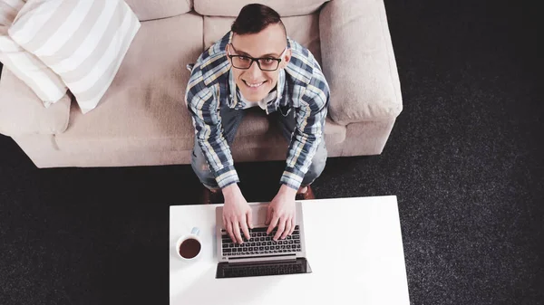 Homem alegre olhando para cima digitando no laptop. Freelanser homem trabalha no aconchegante local de trabalho doméstico. Vista de ângulo alto. Imagem matizada — Fotografia de Stock