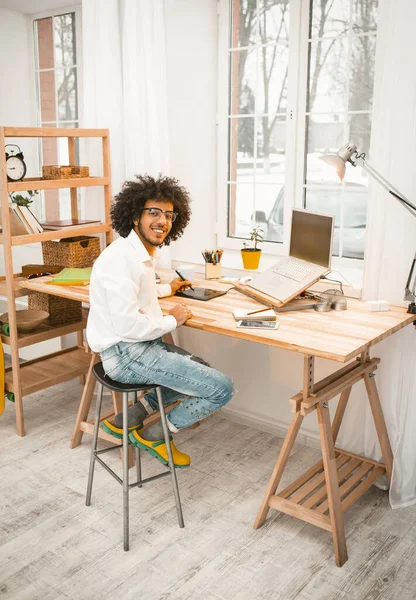 Lugar de trabajo cerca de ventana. Hombre creativo mirando la cámara de trabajo con el ordenador portátil en el interior de la oficina en casa. Concepto independiente. Imagen teñida — Foto de Stock