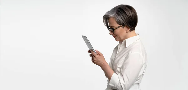 Vue du profil de la femme sérieuse travaillant avec une tablette numérique. Femme d'affaires mature gaie utilisant un ordinateur tablette debout sur fond blanc. Gabarit horizontal pour bannière publicitaire avec espace texte à gauche — Photo