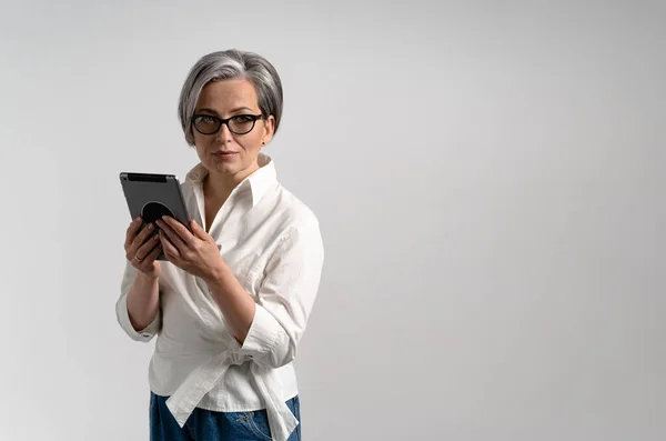 Mulher de negócios cinza bonita detém tablet digital olhando para a câmera enquanto posando no fundo branco. Branco ou modelo para banner com espaço vazio para texto no lado direito — Fotografia de Stock