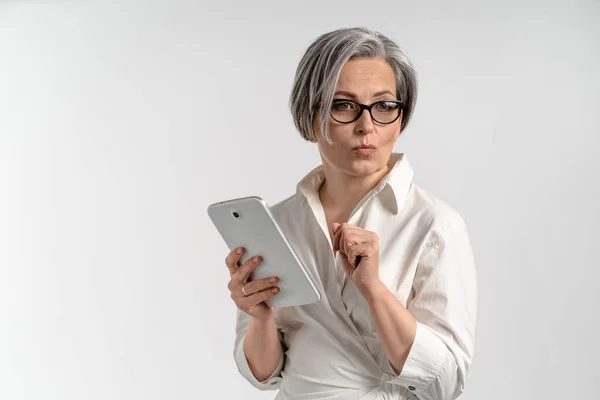 Thoughtfully businesswoman holds white tablet computer. Cheerful Caucasian model in white blouse posing on white background. Bright female portrait in high key — Stock Photo, Image