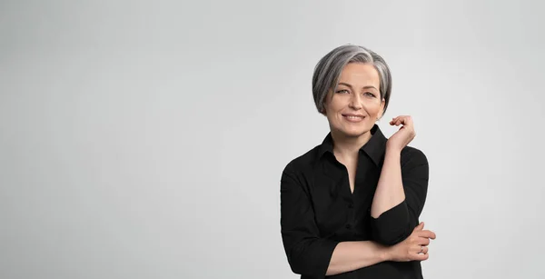 Maturo donna caucasica sorridente affascinante con la mano vicino al viso. Graying donna elegante con taglio di capelli corto bob guarda la fotocamera in posa su sfondo bianco. Vuoto o modello con spazio di testo a sinistra — Foto Stock