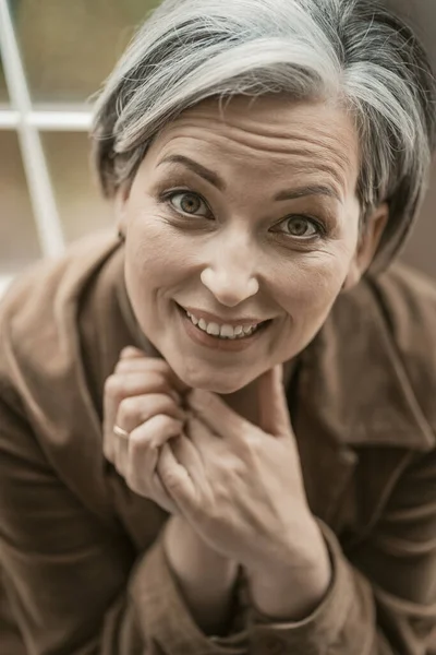 Feliz mulher de meia idade sorri olhando para a câmera. Modelo de cabelos grisalhos caucasiano, retrato de perto. Vista superior. Imagem tonificada — Fotografia de Stock