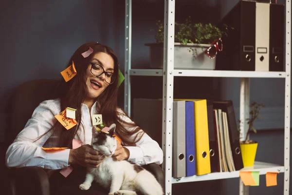 Conceito de procrastinação. Mulher de negócios louca com adesivos de memória colados acariciando um gato. Menina ocupada relaxando no escritório. Imagem matizada — Fotografia de Stock