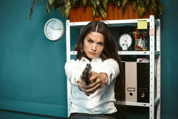Mujer peligrosa con un arma en la oficina. Joven empresaria loca o enojada apuntando directamente a la cámara. Concepto de crisis. Imagen teñida —  Fotos de Stock