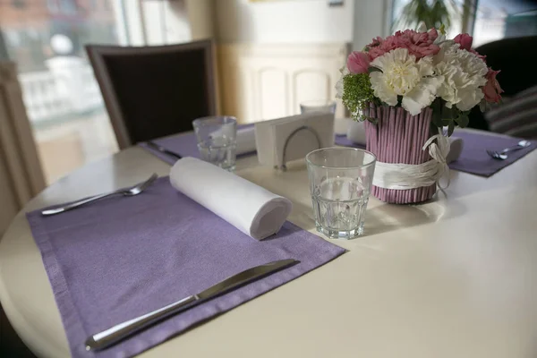 Обідній стіл з милим квітковим декором і фіолетовими серветками в затишному інтер'єрі навпроти вікна. Концепція ювілею або події. Красивий стіл з квітами і серветками — стокове фото