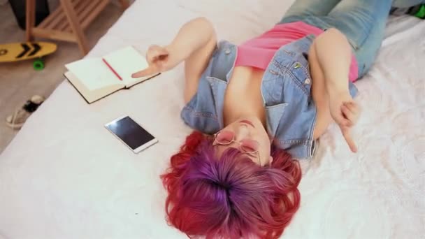 Hipster-Mädchen lag im Bett für einen gesunden Lebensstil. Junge Frauen hören die Musik in rosafarbenen Gläsern. Schönes Modell. Modernes Design — Stockvideo